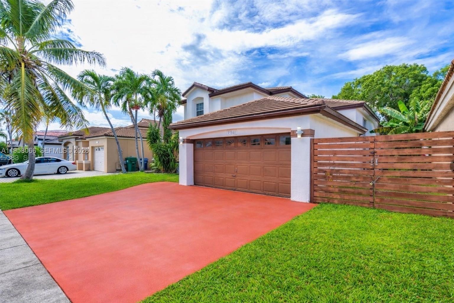 A two-story house with a brown garage door, red driveway, and wooden privacy fence — 13249 NW 9th Ln, Miami FL 33182, MIAMI, FL