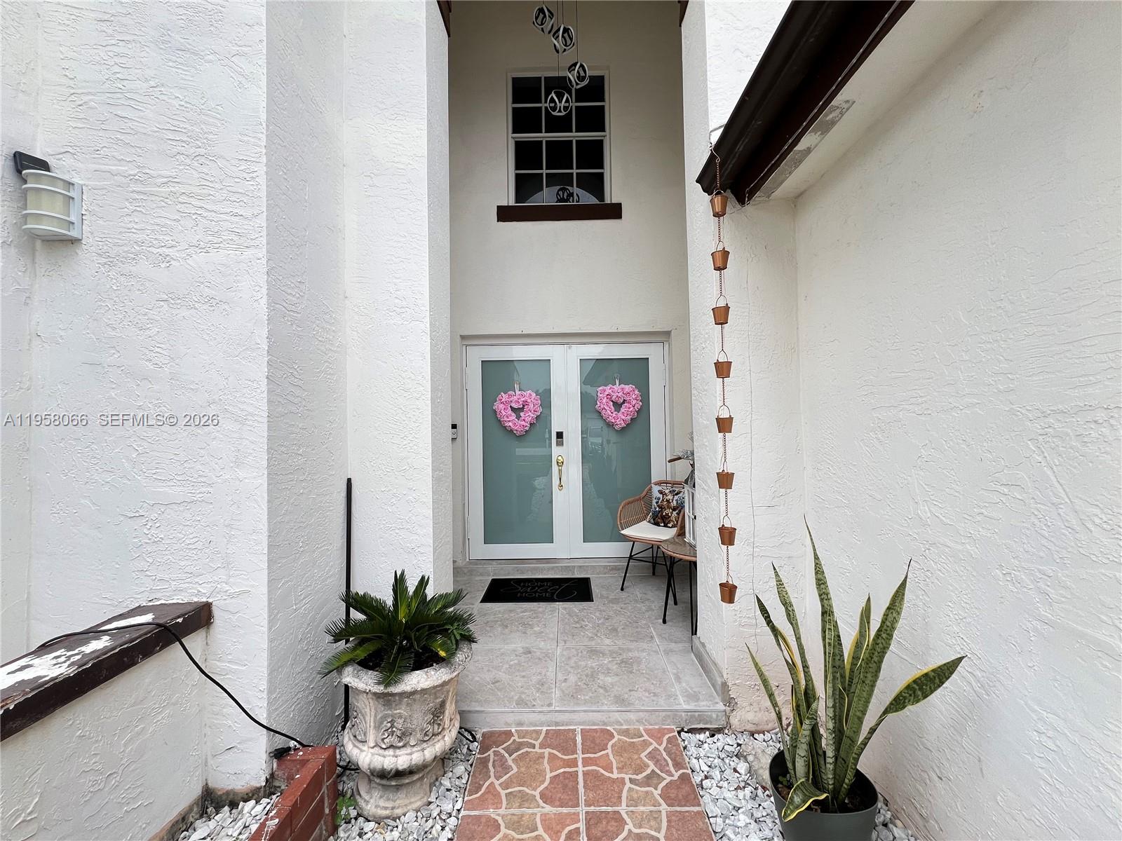 A white stucco entryway features double glass doors with heart wreaths and a rain chain — 13249 NW 9th Ln, Miami FL 33182, MIAMI, FL