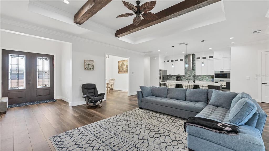 An open-concept living room features a blue sectional sofa, wood flooring, and exposed ceiling beams — 6706 TANEYTOWN STREET, NORTH PORT, FL