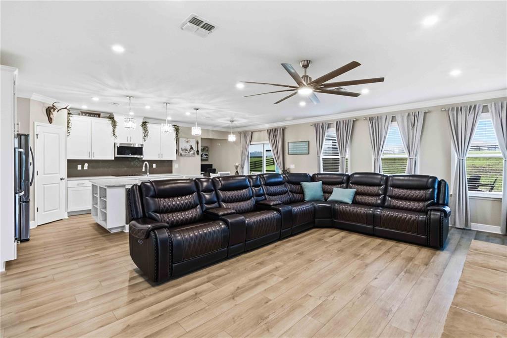 A spacious open-concept living room and kitchen featuring a large sectional sofa and wood flooring — 10007 DOLPHIN GULL CIRCLE, THONOTOSASSA, FL