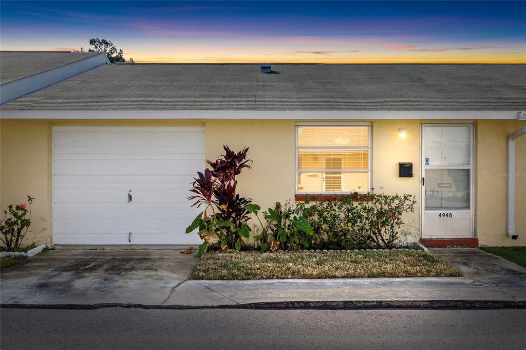 A single-story yellow house exterior features a white garage door, a window, and a door — 4948 GETNER STREET, NEW PORT RICHEY, FL