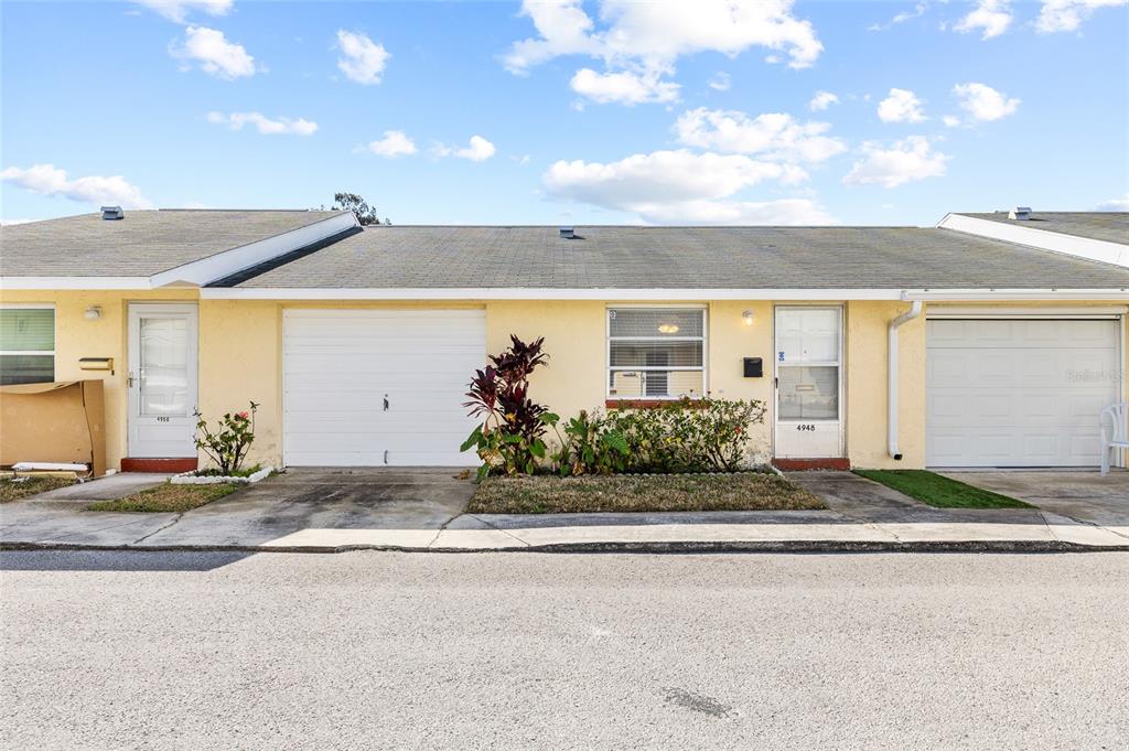 A single-story yellow townhouse with a white garage door, a front door, and a small garden — 4948 GETNER STREET, NEW PORT RICHEY, FL