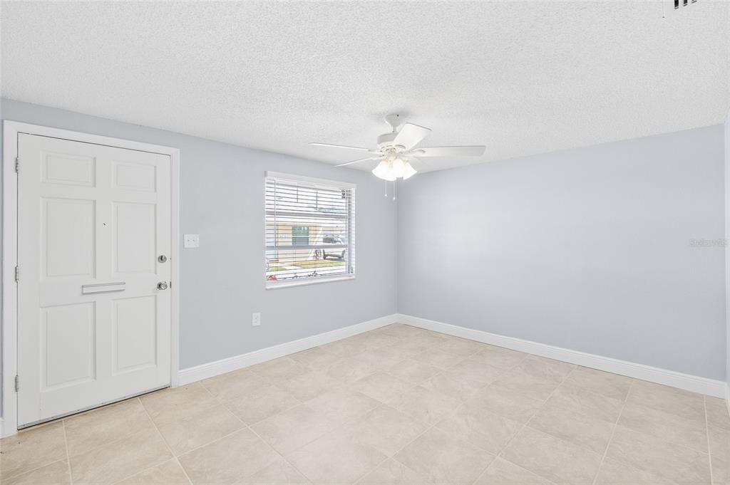 An empty room with light blue walls, tile flooring, a ceiling fan, and a door — 4948 GETNER STREET, NEW PORT RICHEY, FL