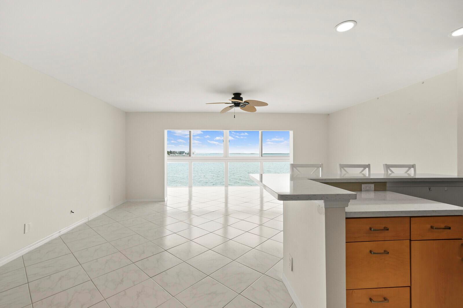 An open-concept room features light tile flooring, a kitchen island, and large windows overlooking water — 400 Wilma Circle # 207, Riviera Beach FL 33404, RIVIERA BEACH, FL