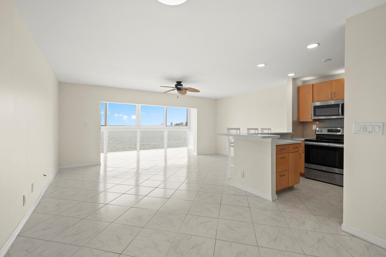 An open-concept living area features light tile flooring, a kitchen island, and large water-view windows — 400 Wilma Circle # 207, Riviera Beach FL 33404, RIVIERA BEACH, FL