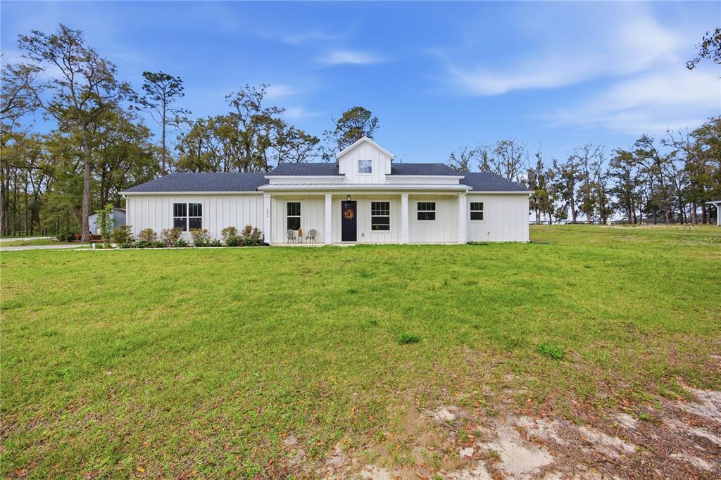 A white farmhouse with a dark roof and a front porch sits on a lawn — 5070 SW 129TH COURT, OCALA, FL