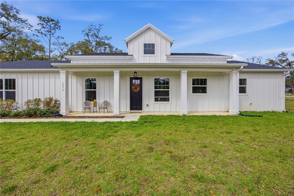 A white farmhouse-style home features a covered front porch, board-and-batten siding, and a black door — 5070 SW 129TH COURT, OCALA, FL