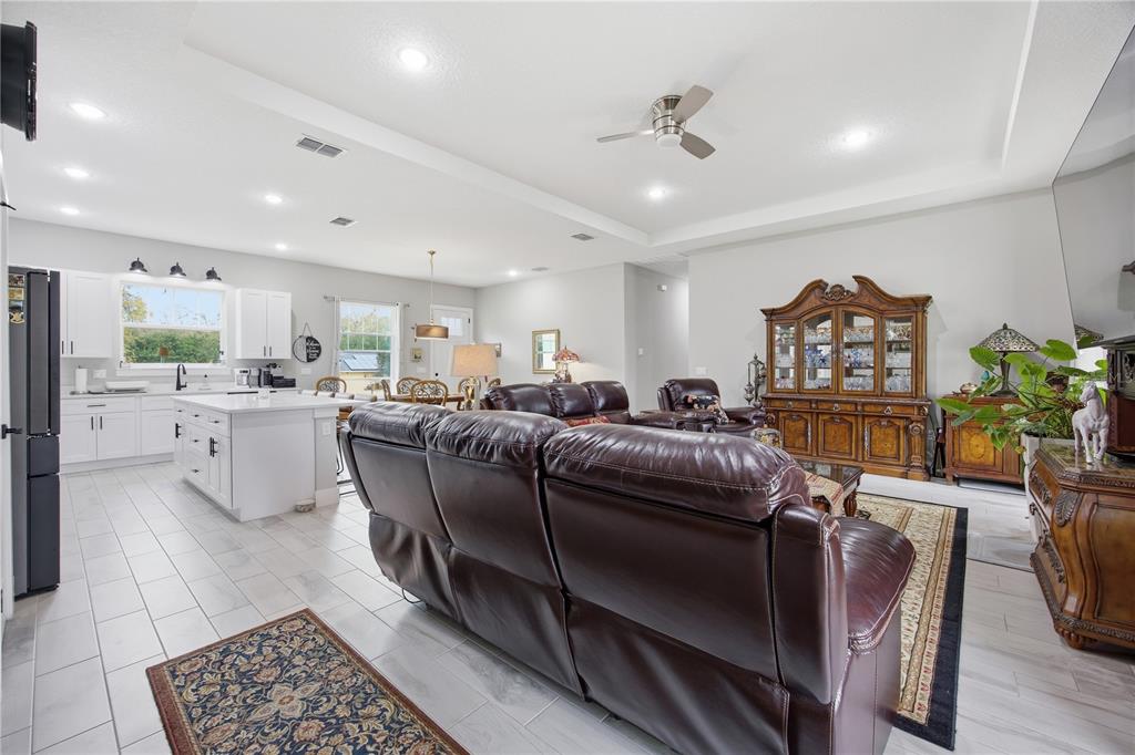 An open-concept living room and kitchen featuring white cabinetry, tile flooring, and leather furniture — 5070 SW 129TH COURT, OCALA, FL
