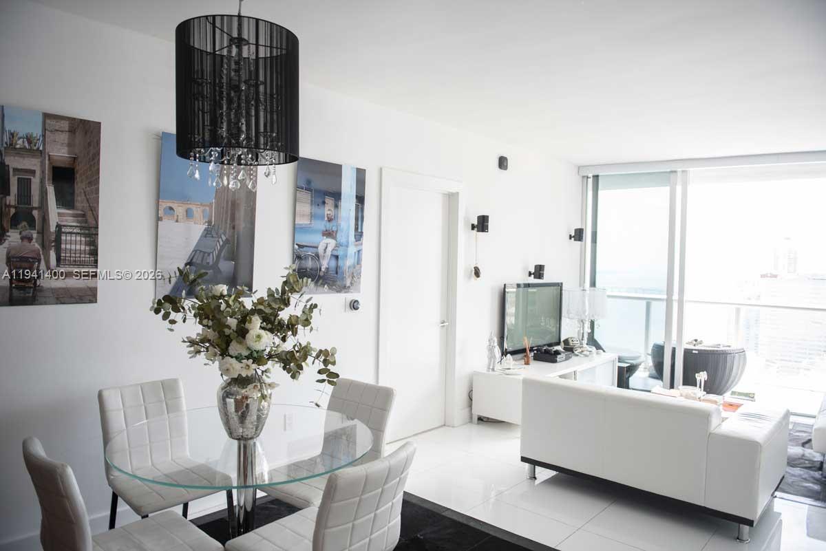 A modern dining and living area features a glass table, white chairs, and floor-to-ceiling windows — 495 Brickell Ave # 3805, Miami FL 33131, MIAMI, FL