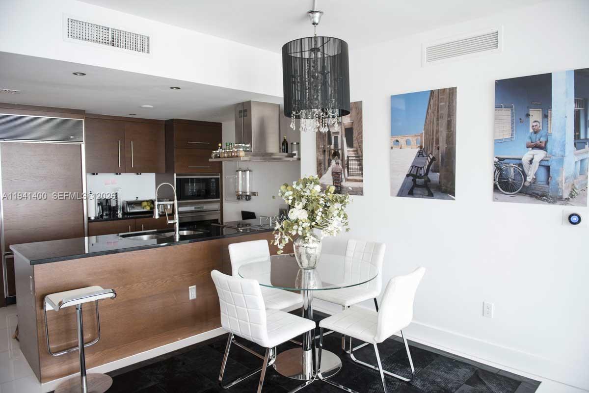 A modern kitchen features dark wood cabinetry, a breakfast bar, and a glass dining table — 495 Brickell Ave # 3805, Miami FL 33131, MIAMI, FL