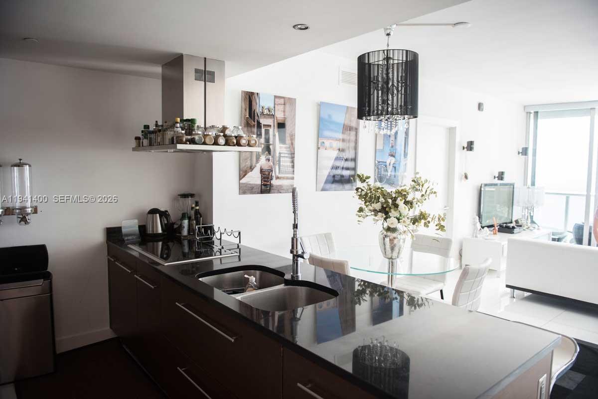 A modern kitchen features dark cabinetry, black countertops, a stainless steel hood, and dining area — 495 Brickell Ave # 3805, Miami FL 33131, MIAMI, FL