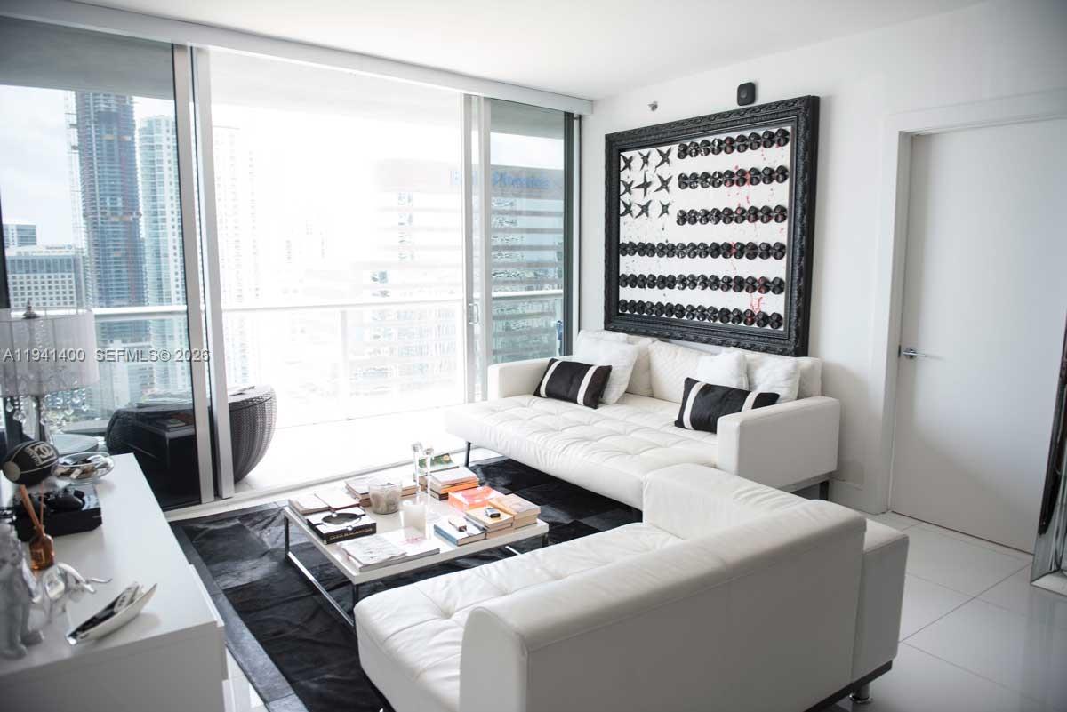 A modern living room features a white sectional sofa, a coffee table, and a large artwork — 495 Brickell Ave # 3805, Miami FL 33131, MIAMI, FL