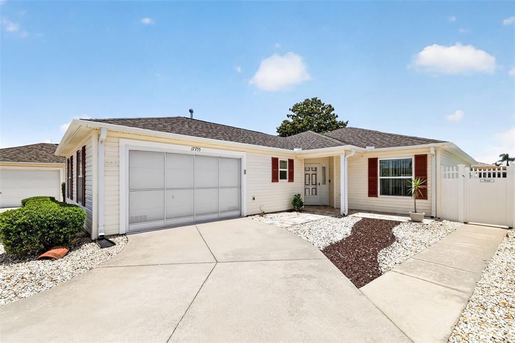 A single-story house with beige siding, a white garage door, and a concrete driveway — 17755 SE 84TH SHELDON TERRACE, THE VILLAGES, FL