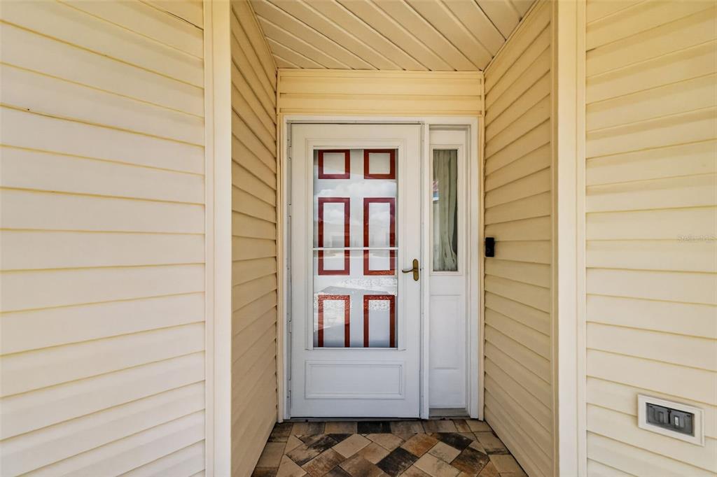 A white front door with glass panels is set within a light-colored vinyl-sided entryway — 17755 SE 84TH SHELDON TERRACE, THE VILLAGES, FL