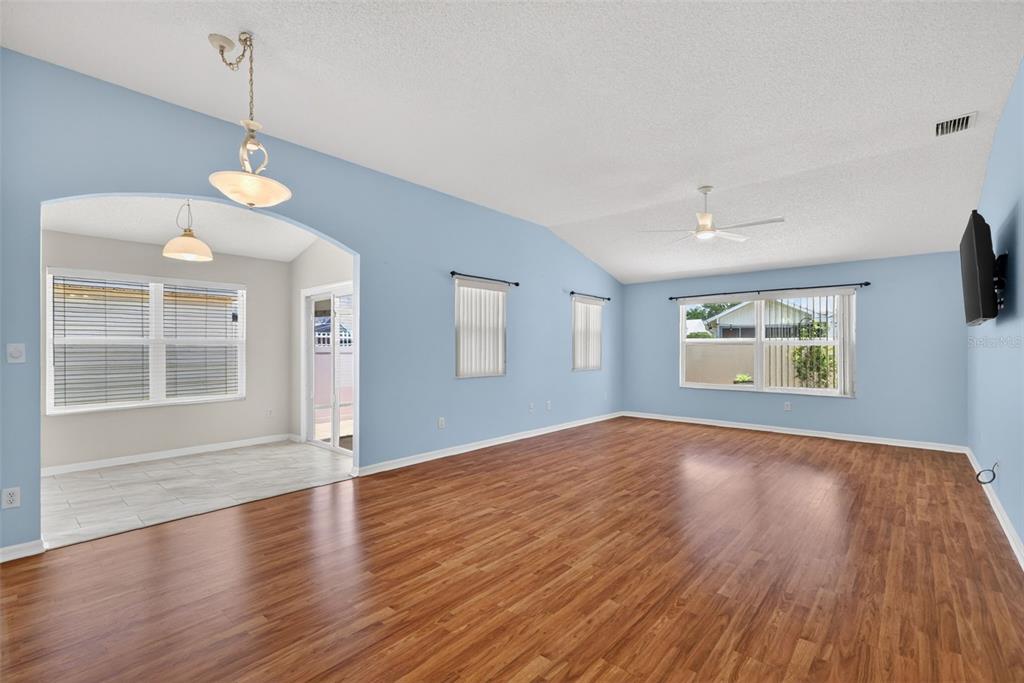 A living room with light blue walls, wood flooring, and an adjacent dining area — 17755 SE 84TH SHELDON TERRACE, THE VILLAGES, FL