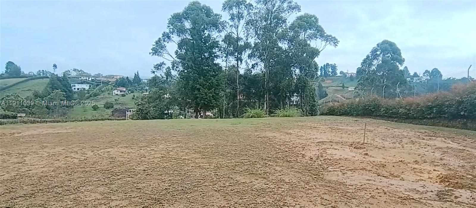 A large, open, grassy lot with trees and distant houses under a cloudy sky — Vereda Mampuesto Sector Garrido #14, C Colombia, C