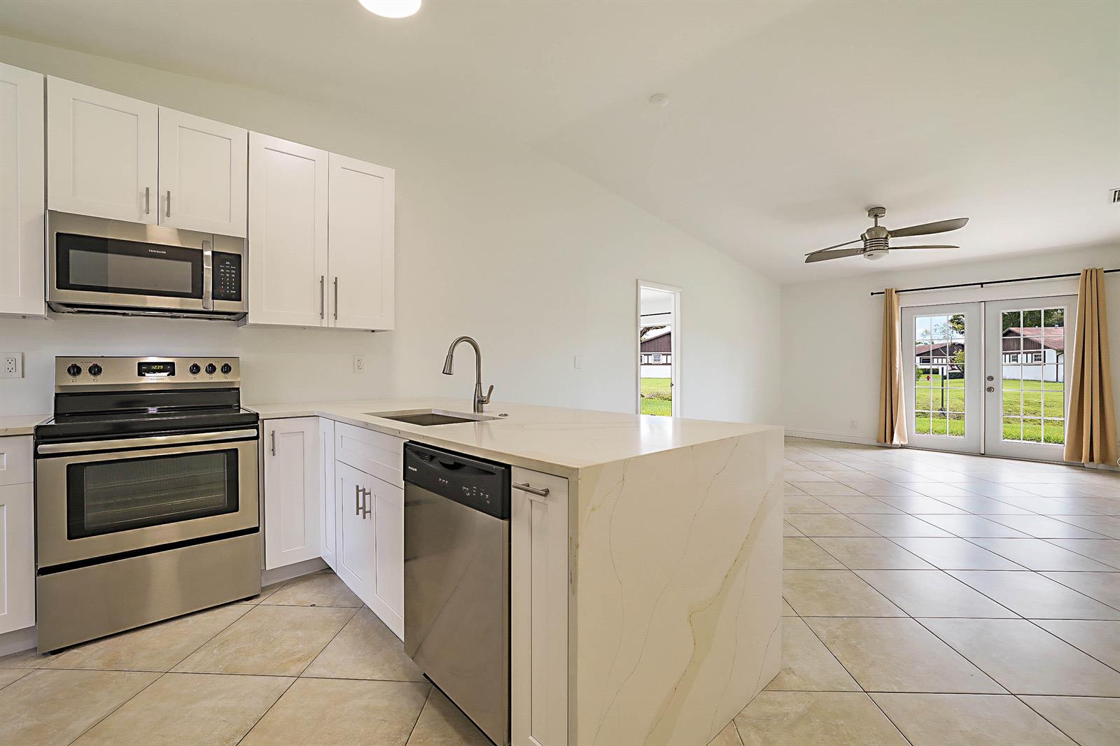 A kitchen with white cabinets, stainless steel appliances, and a waterfall island overlooks a living area — 5241 Breadfruit Circle, Delray Beach FL 33484, DELRAY BEACH, FL