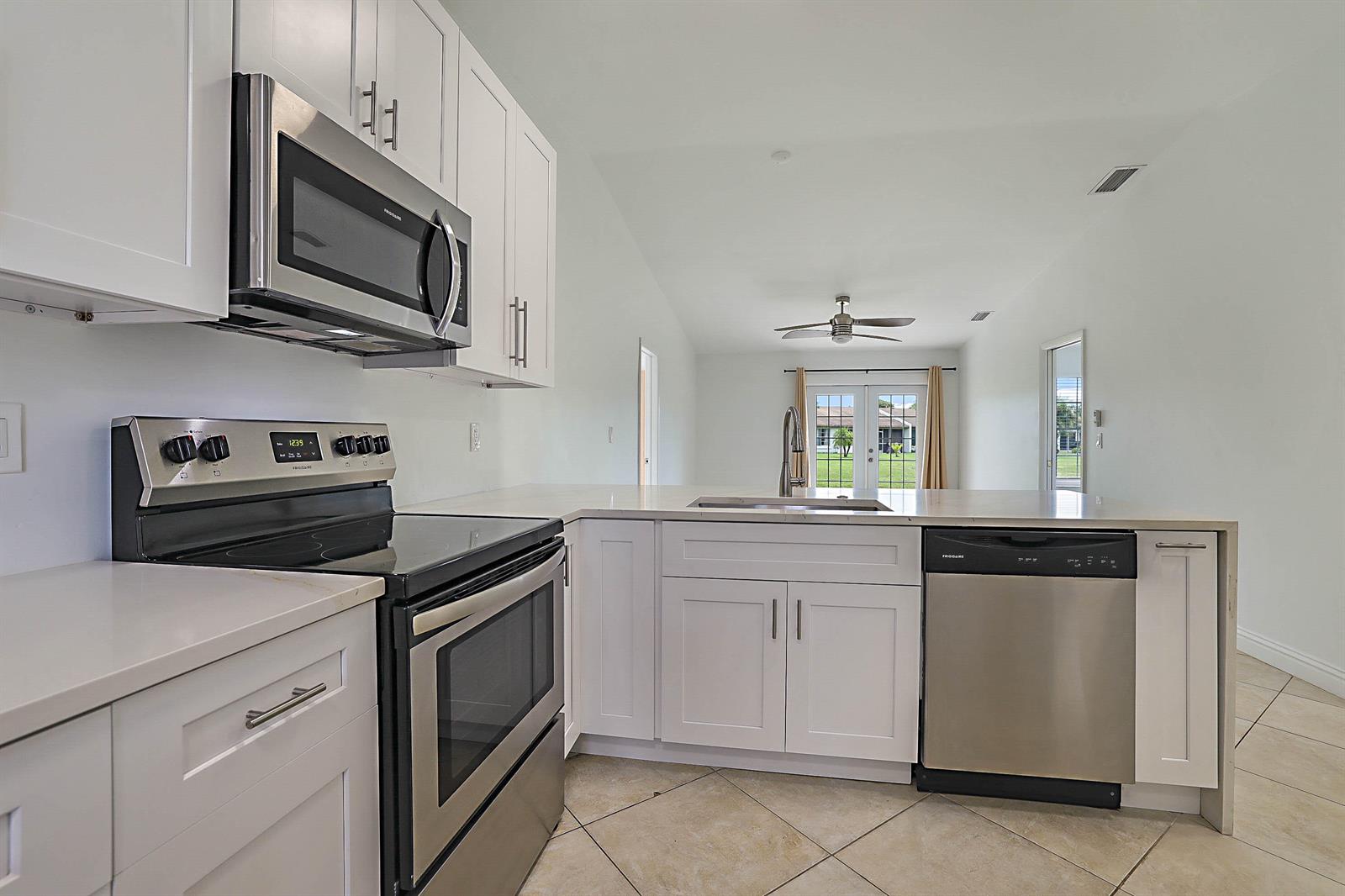 A kitchen with white cabinets, stainless steel appliances, and a view of a living area — 5241 Breadfruit Circle, Delray Beach FL 33484, DELRAY BEACH, FL