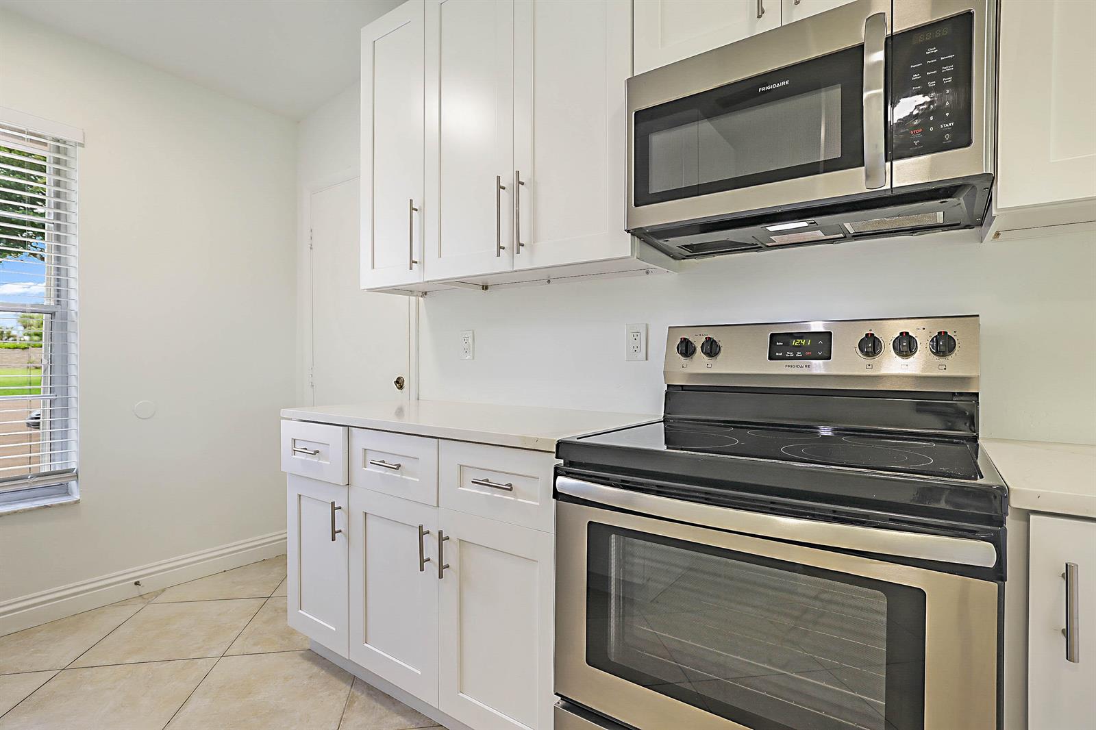 A kitchen features white cabinets, stainless steel appliances, and a window with blinds — 5241 Breadfruit Circle, Delray Beach FL 33484, DELRAY BEACH, FL