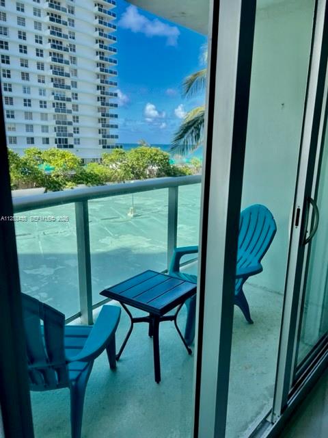 A balcony with two blue chairs and a small table overlooking a beach and building — 3801 S Ocean Dr # 3C, Hollywood FL 33019, HOLLYWOOD, FL