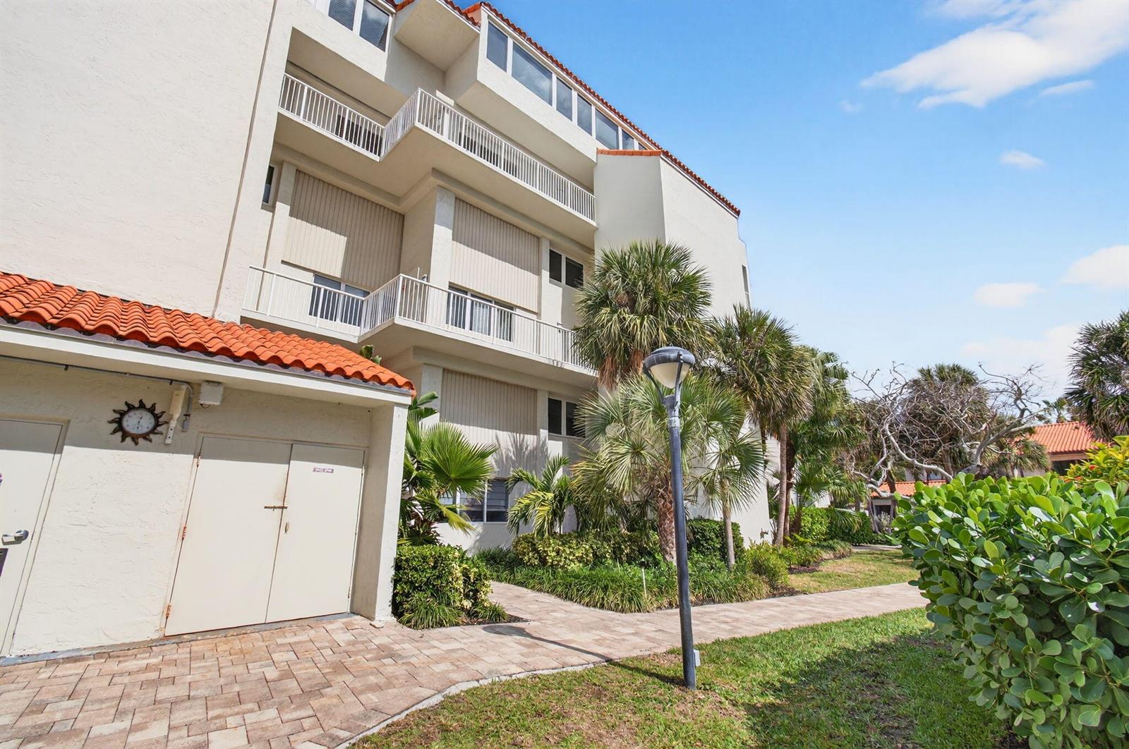 A multi-story building with balconies and a tiled roof stands next to a paved walkway — 3908 S Ocean Boulevard # 127, Highland Beach FL 33487, HIGHLAND BEACH, FL