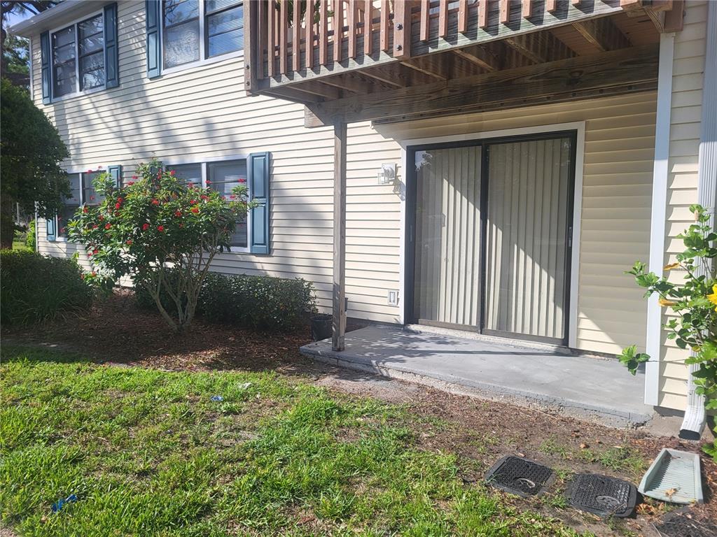 A beige building exterior features a sliding glass door, a concrete patio, and landscaping — 140 HUNTER LAKE DRIVE UNIT F, OLDSMAR, FL
