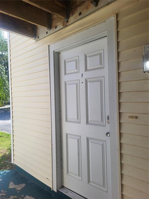 A white six-panel door labeled with an F is set into yellow horizontal siding — 140 HUNTER LAKE DRIVE UNIT F, OLDSMAR, FL