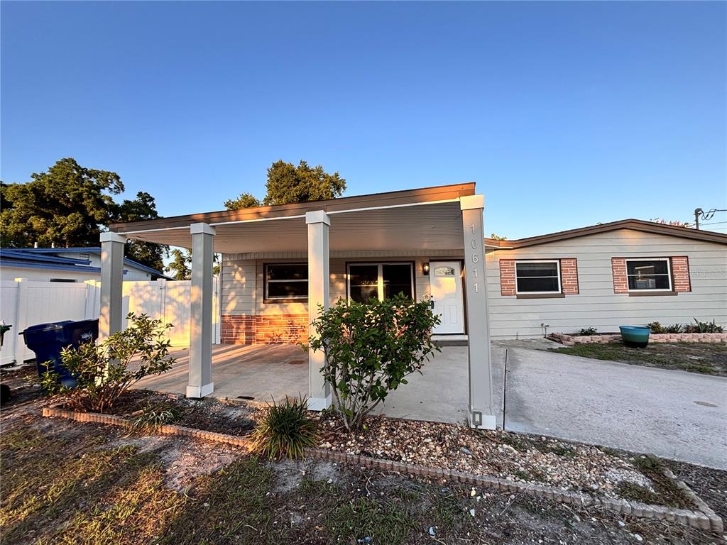 A single-story house features a covered carport, light-colored siding, and a small front garden bed — 10611 N ALTMAN STREET, TAMPA, FL
