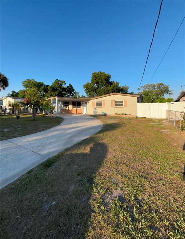 A single-story house with a beige exterior, a curved driveway, and a white privacy fence — 10611 N ALTMAN STREET, TAMPA, FL
