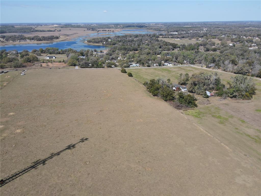 An aerial view shows a large, dry grassy field adjacent to a wooded residential area — 10740 FORT KING ROAD, DADE CITY, FL
