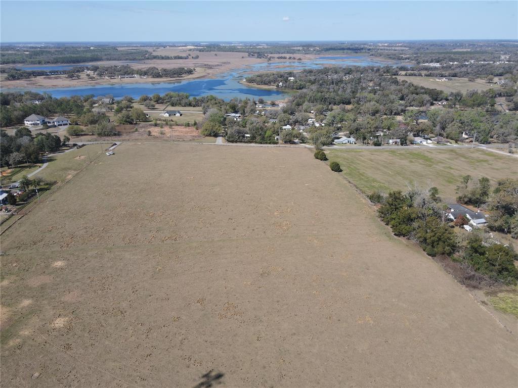 An aerial view shows a large, open, dry grassy field bordered by trees and houses — 10740 FORT KING ROAD, DADE CITY, FL