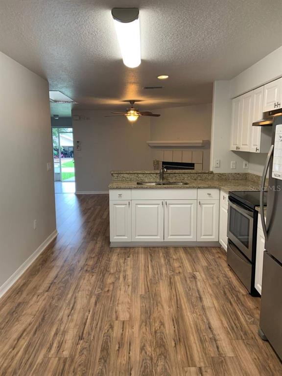 A kitchen with white cabinets and granite countertops overlooks a living area with wood flooring — 38 LINDSAY DRIVE UNIT A, PALM COAST, FL