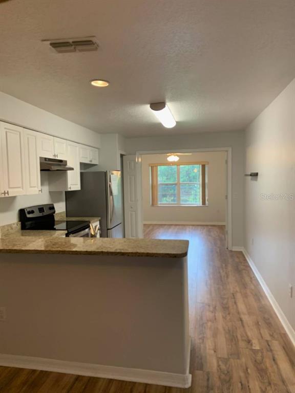 A kitchen with white cabinets and granite countertops opens into a dining area with wood-look flooring — 38 LINDSAY DRIVE UNIT A, PALM COAST, FL