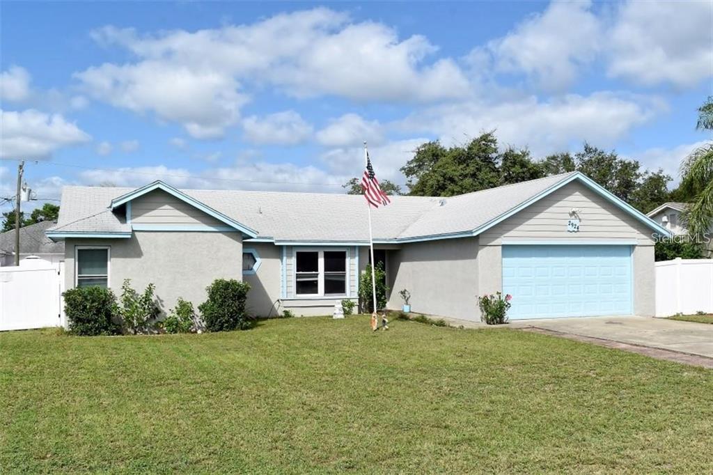 A single-story house with a light gray exterior, a two-car garage, and an American flag — 2924 GIMLET DRIVE, DELTONA, FL