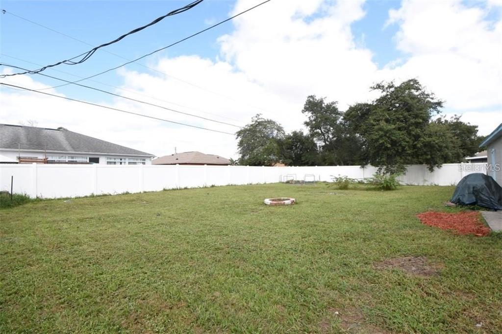 A grassy backyard features a white vinyl fence, a fire pit, and mature trees — 2924 GIMLET DRIVE, DELTONA, FL