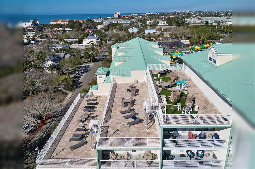 An aerial view shows a building rooftop terrace with lounge chairs, tables, and artificial turf — 399 2ND STREET UNIT 416, INDIAN ROCKS BEACH, FL