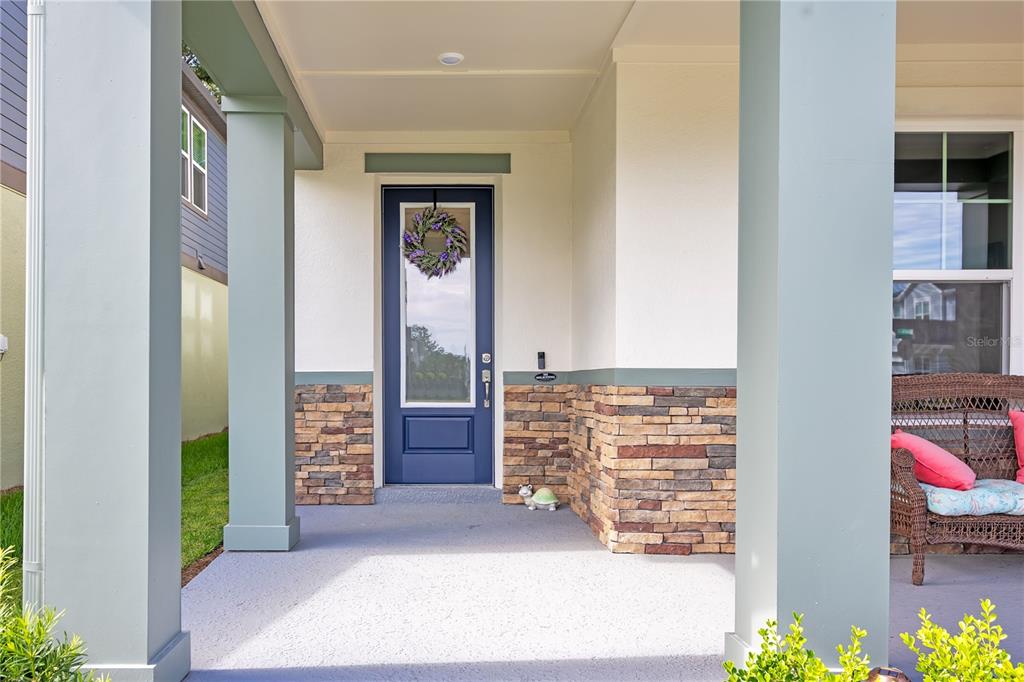 A covered front porch features a blue door, stone veneer siding, and a wicker chair — 5972 SACRED OAK AVENUE, MOUNT DORA, FL