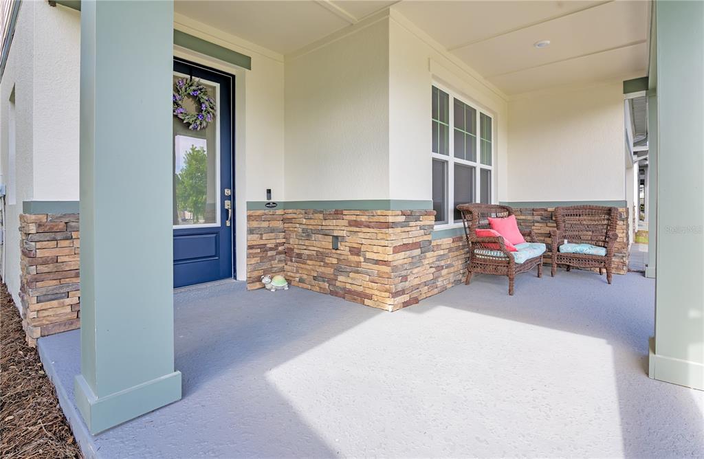 A covered front porch features stone siding, a blue door, and two wicker chairs — 5972 SACRED OAK AVENUE, MOUNT DORA, FL
