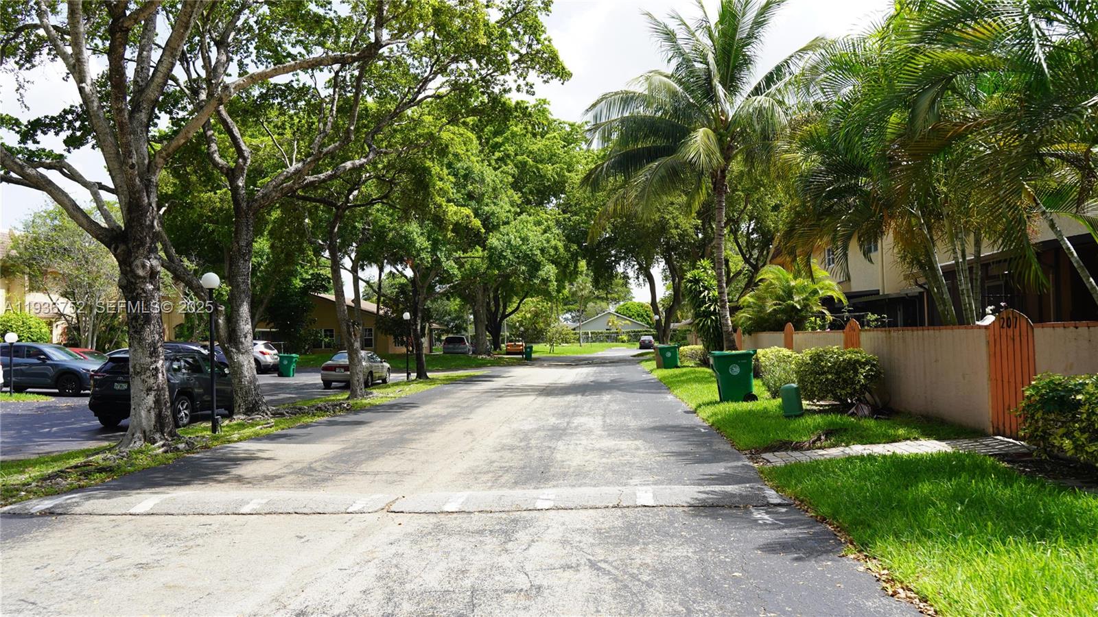 A paved residential street is lined with mature trees, parked cars, and green trash bins — 7175 Nova Dr # 204, Davie FL 33317, DAVIE, FL