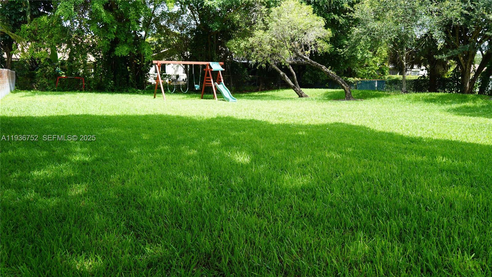 A large, grassy backyard features a wooden swing set with a slide and mature trees — 7175 Nova Dr # 204, Davie FL 33317, DAVIE, FL