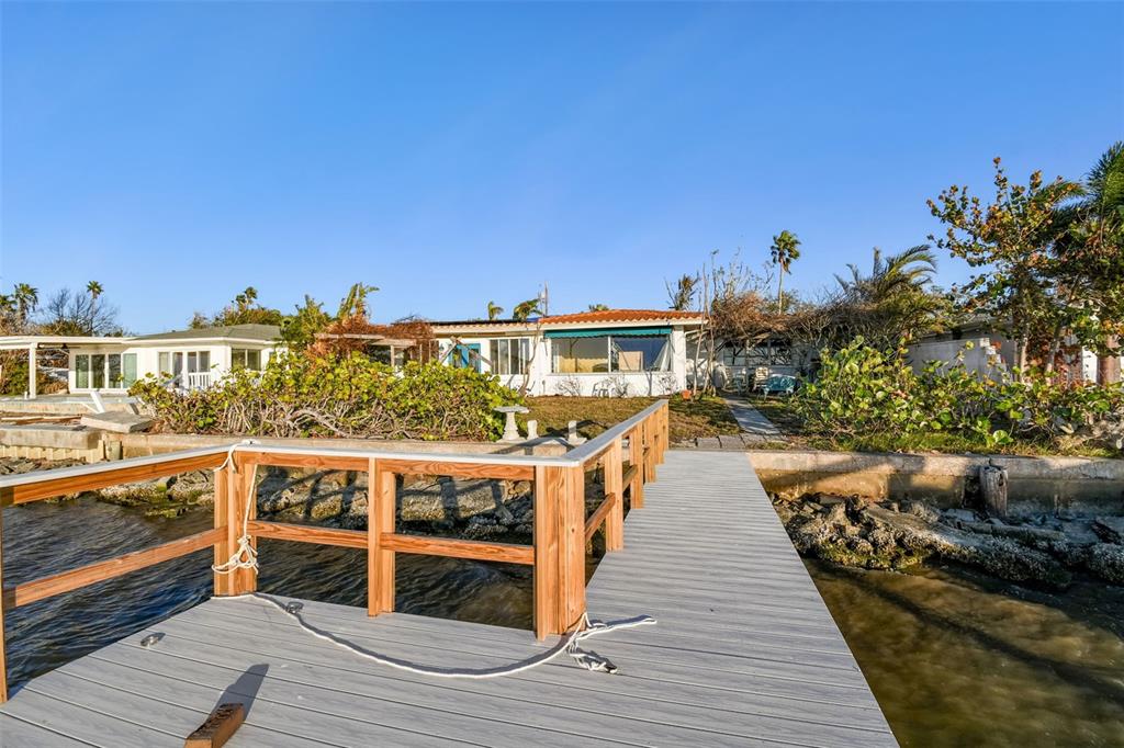 A wooden dock extends toward a waterfront house with a white exterior and green awning — 1836 VENETIAN POINT DRIVE, CLEARWATER, FL