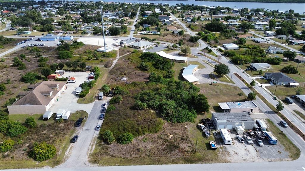 An aerial view shows a vacant lot surrounded by commercial buildings, parking areas, and vegetation — 3104 CARDIFF STREET, PUNTA GORDA, FL