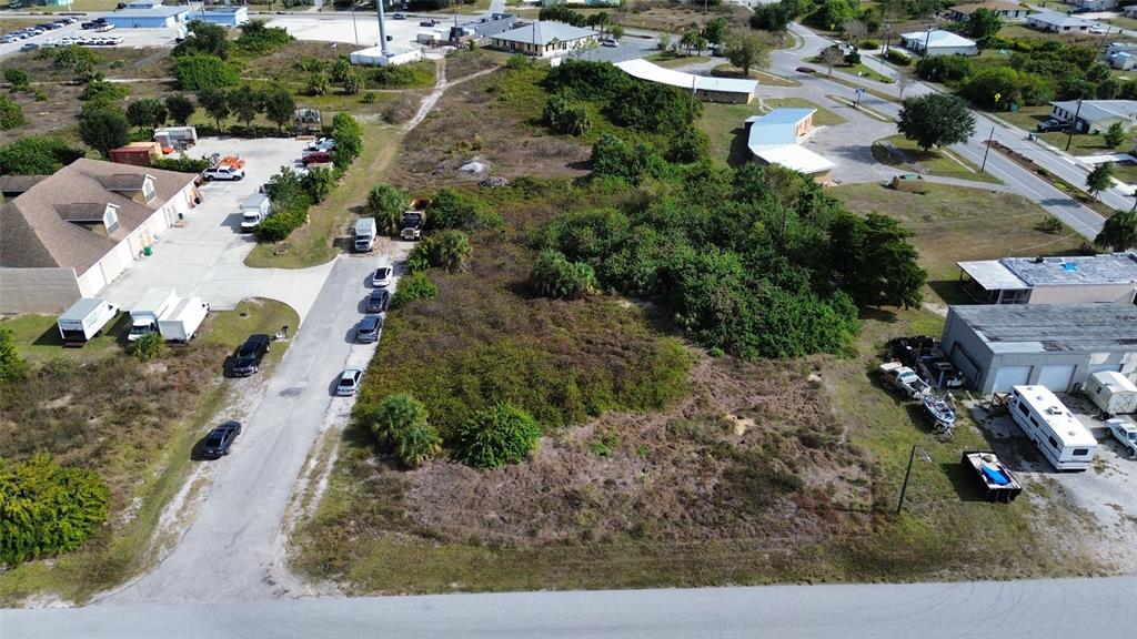 An aerial view shows a vacant, brush-covered lot situated between commercial buildings and paved roads — 3104 CARDIFF STREET, PUNTA GORDA, FL