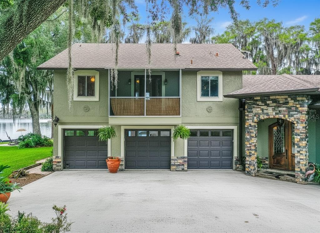 A two-story house with three garage doors, a screened balcony, and a stone-accented entryway — 6850 HUNT ROAD, GROVELAND, FL