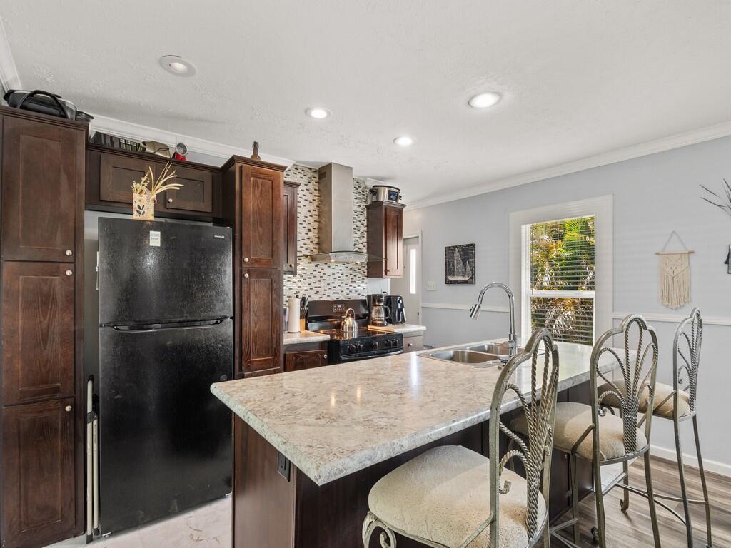 A kitchen features dark wood cabinets, a black refrigerator, a stone-topped island, and bar stools — 309 Mockingbird Avenue, Fort Pierce FL 34982, FORT PIERCE, FL