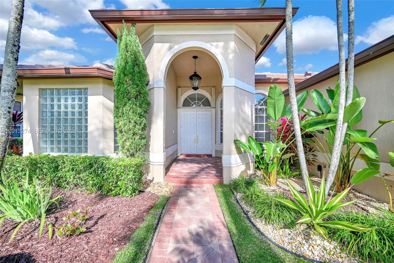 The exterior of a house features a brick walkway leading to a covered arched entryway — 2553 Jardin Manor, Weston FL 33327, WESTON, FL