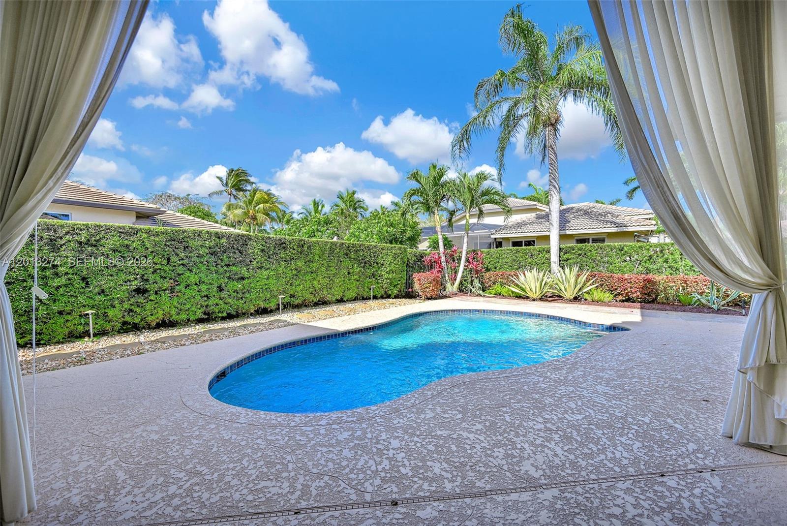 A backyard features a kidney-shaped swimming pool surrounded by a concrete patio and hedges — 2553 Jardin Manor, Weston FL 33327, WESTON, FL