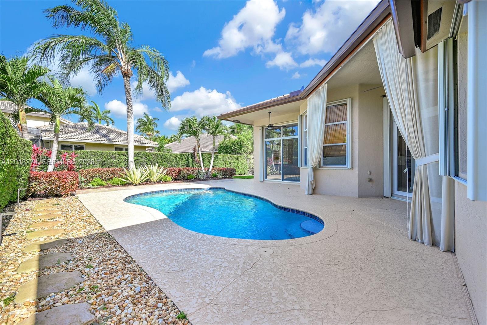 A backyard features a kidney-shaped swimming pool, a covered patio, and surrounding tropical landscaping — 2553 Jardin Manor, Weston FL 33327, WESTON, FL