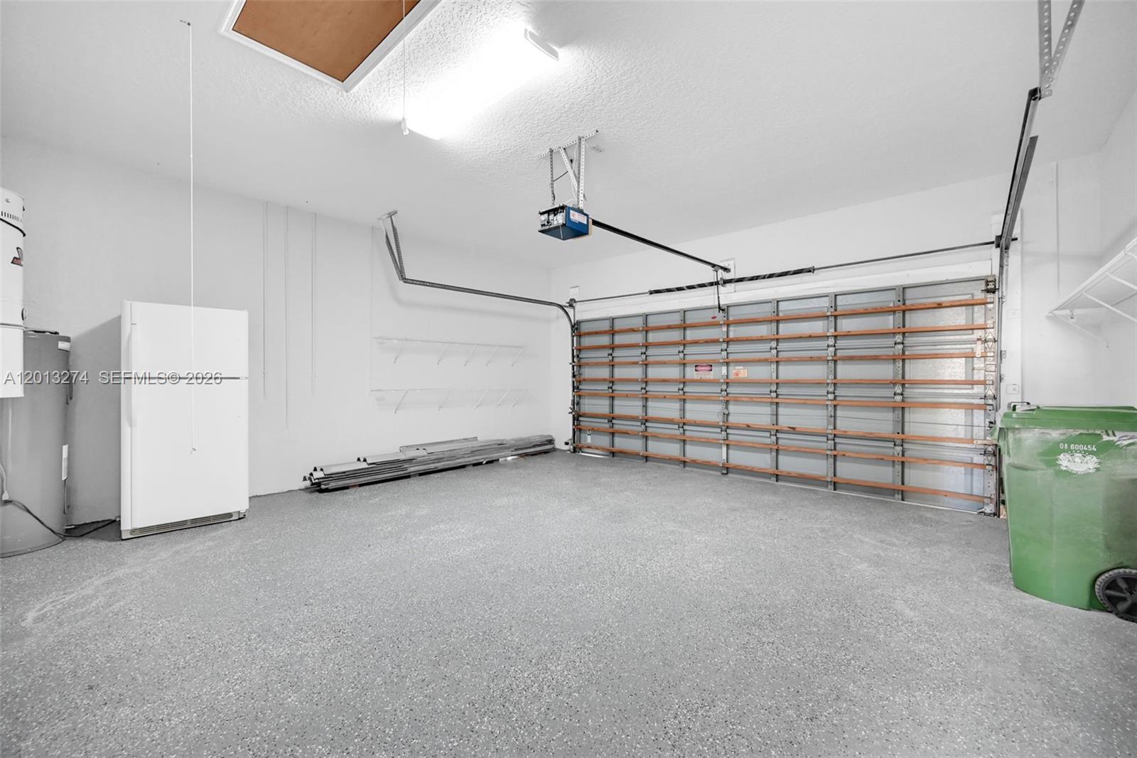A garage features a speckled concrete floor, a white refrigerator, and a green trash bin — 2553 Jardin Manor, Weston FL 33327, WESTON, FL