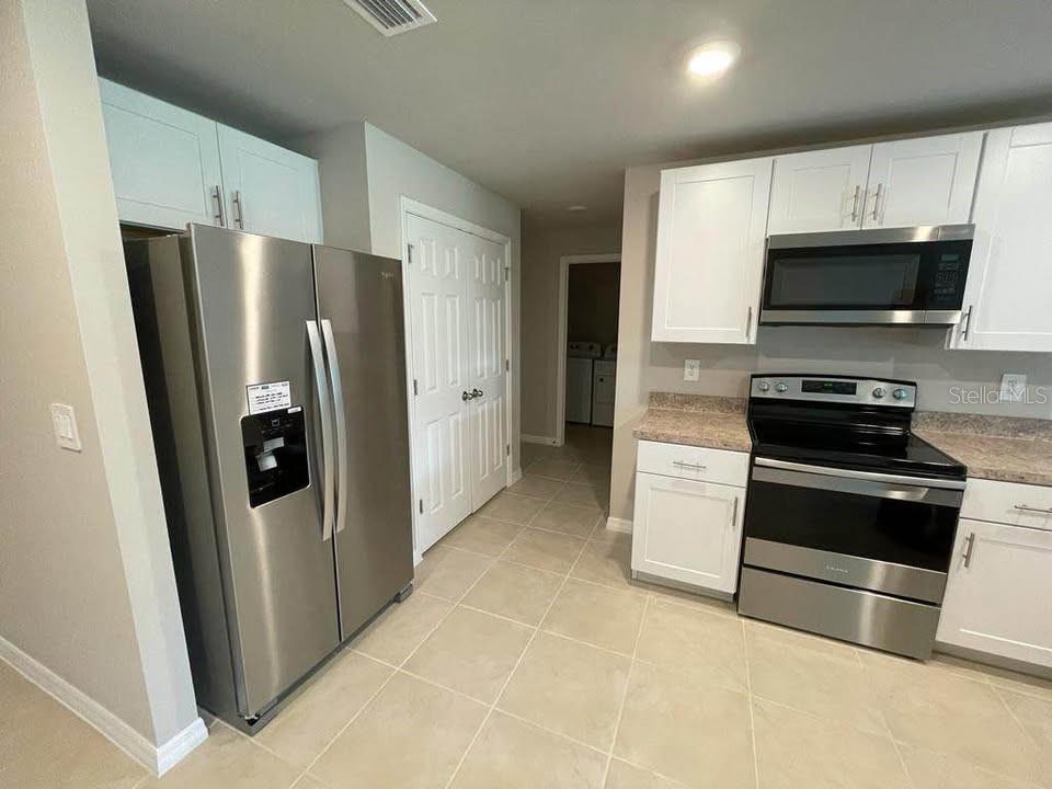 A kitchen with stainless steel appliances, white cabinets, and light-colored tile flooring — 456 MACARTHUR DRIVE, PORT CHARLOTTE, FL